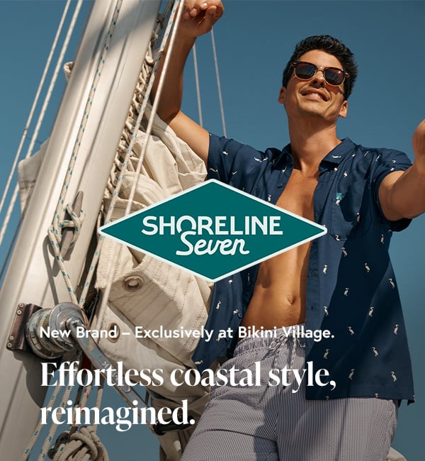 Man aboard a sailboat, wearing volley swim shorts and a Shoreline Seven shirt. 