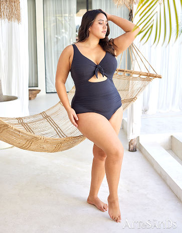 Woman standing in front of a hammock wearing a textured black one‑piece swimsuit by Artesands